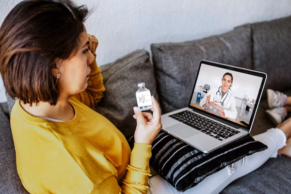 Physician smiling and waving at webcam wearing a headset.